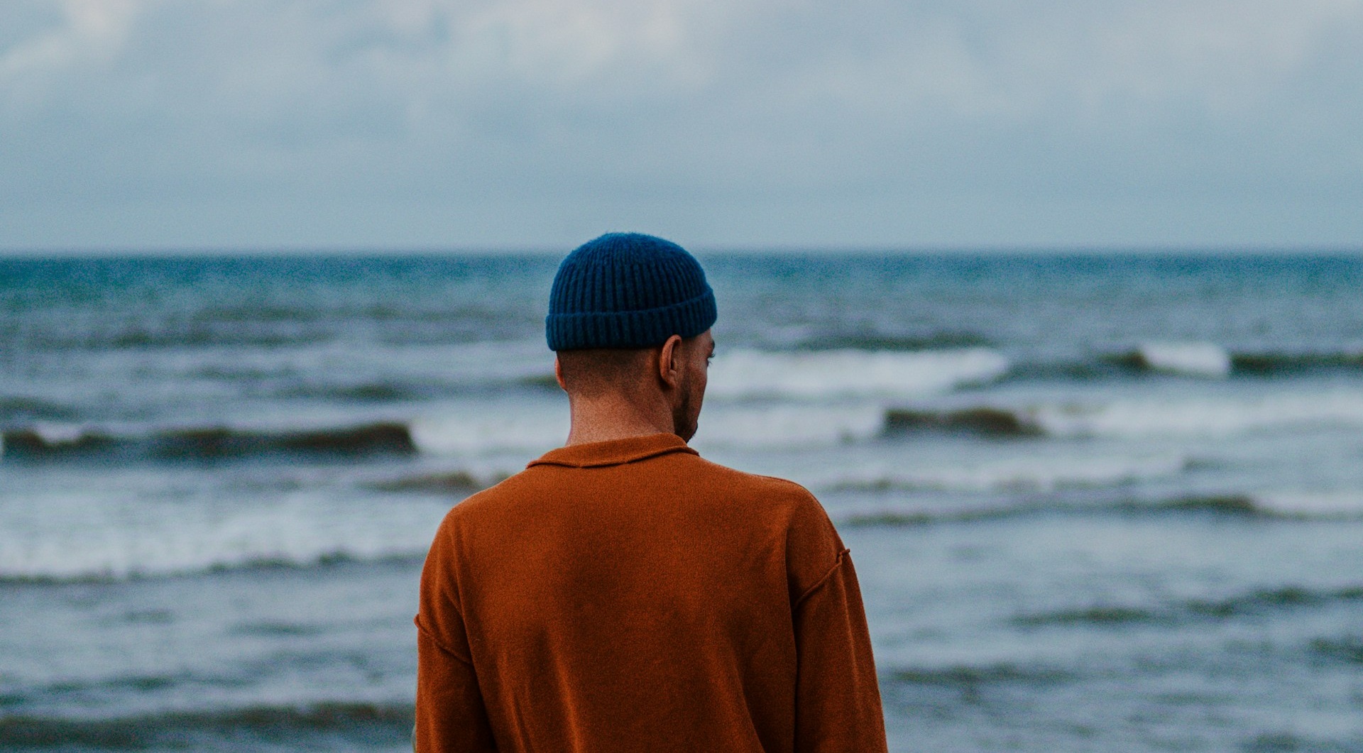 Man looks at ocean wearing blue beanie